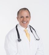 A smiling male doctor wearing a white lab coat, yellow tie, and stethoscope around his neck stands against a white background.